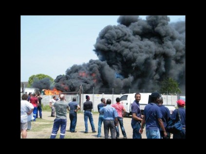 Community members watch as a large cloud of black smoke rises from a site in Alton on Friday